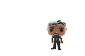 A Funko Pop figure stands against a plain white background. The figure has a bandana tied around its head, wearing a black outfit with gold accessories and has a serious facial expression.