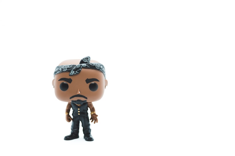 A vinyl figurine of a character wearing a black outfit with a bandana on its head. The figure is stylized, with exaggerated facial features and stands against a plain white background.