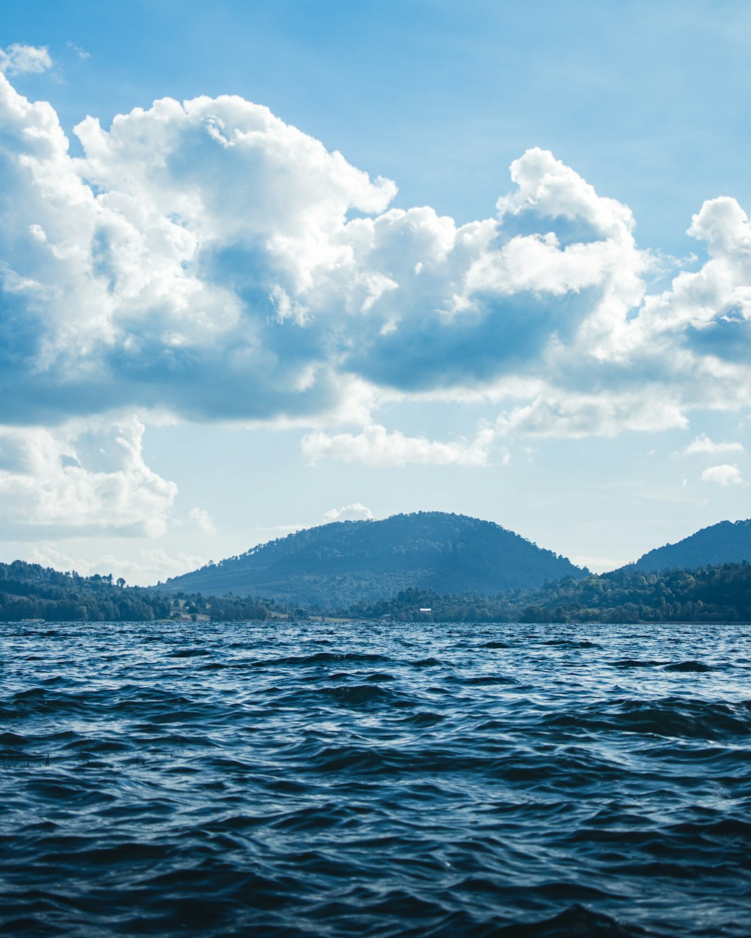 body of water near mountain under white clouds during daytime