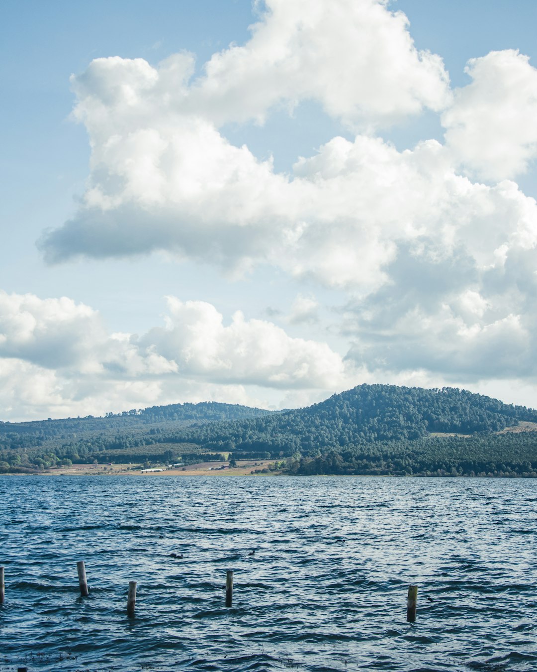 body of water near mountain under white clouds during daytime