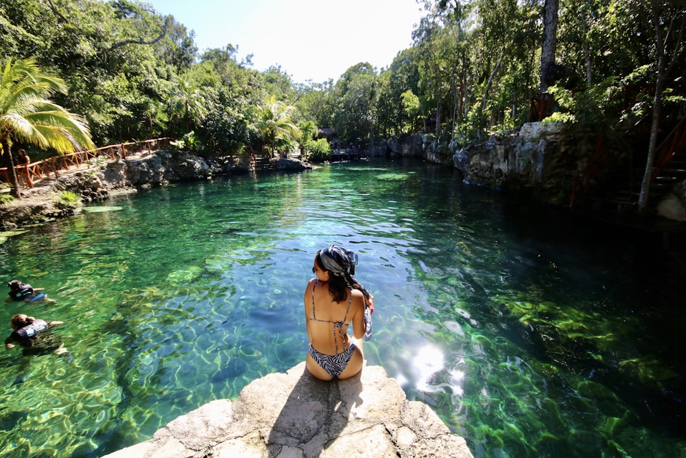 mulher no biquíni preto de pé na rocha perto do rio durante o dia