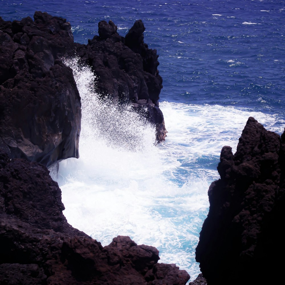Les vagues de l’océan s’écrasent sur la formation de roches noires pendant la journée