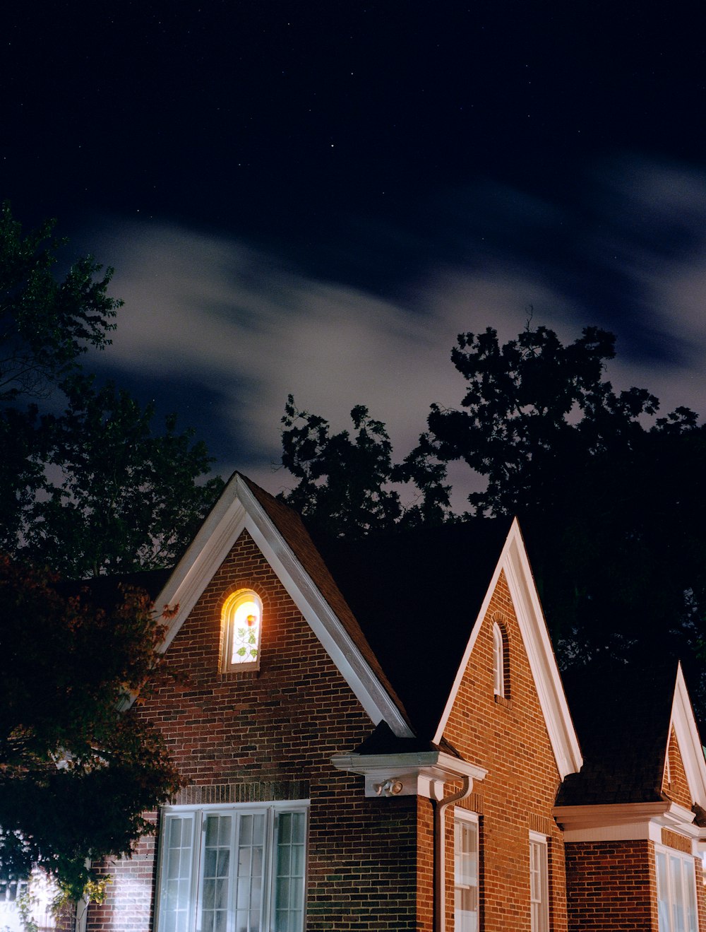 brown and white house near green trees under dark sky