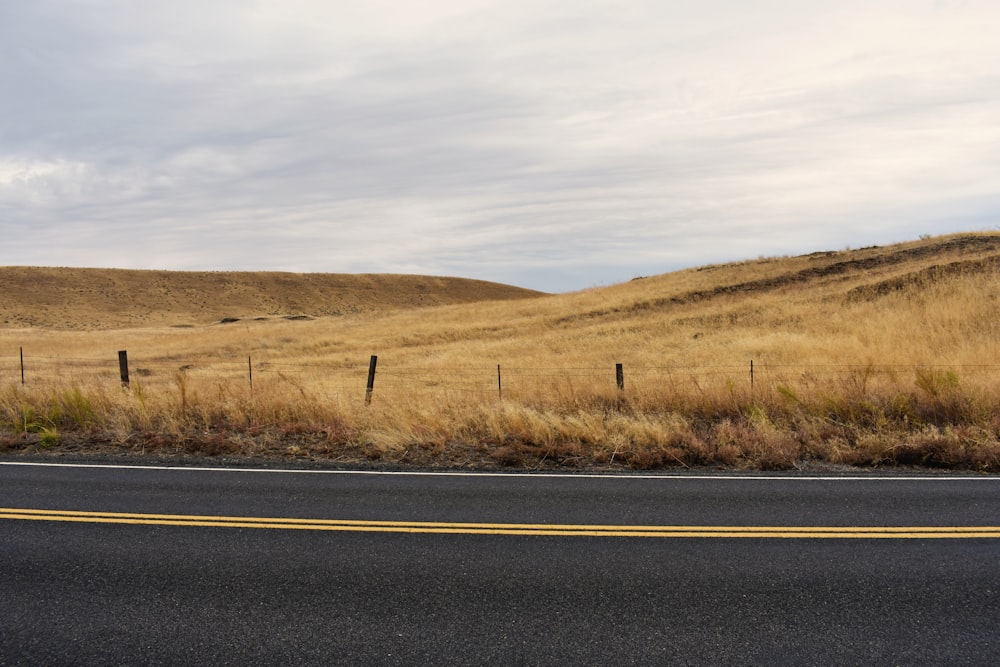 gray asphalt road in between brown grass field during daytime