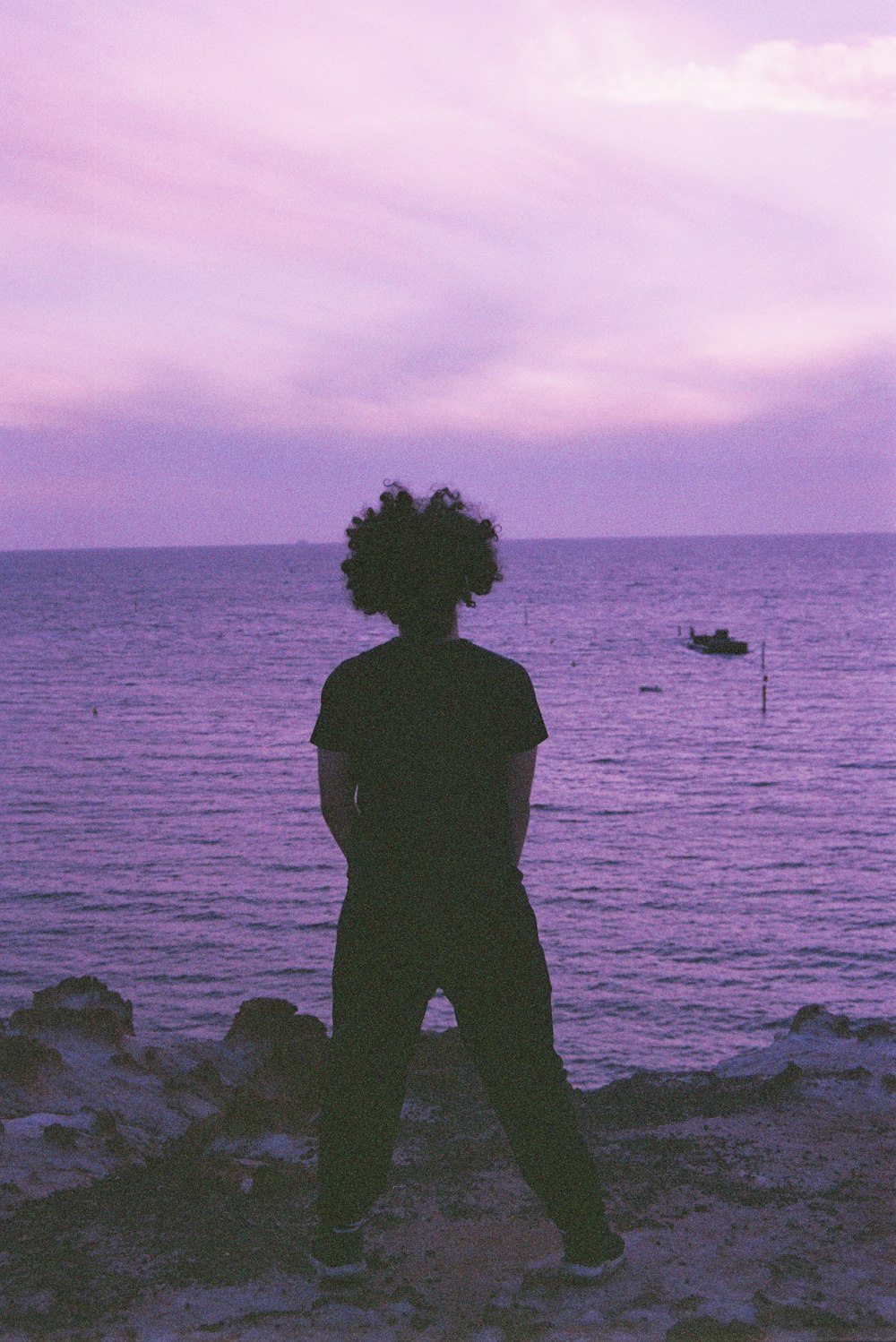 silhouette of person standing on rock near body of water during sunset