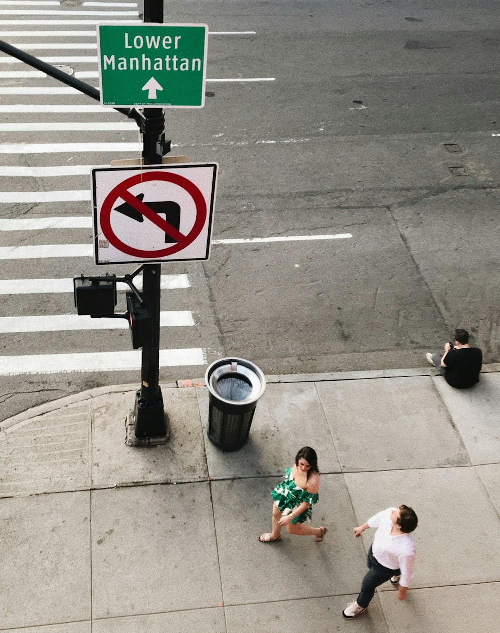 woman in white tank top sitting on sidewalk beside pedestrian lane during daytime