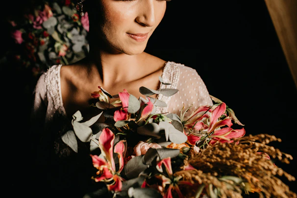 Softly lit close-up of a woman gently holding a blooming garden flower, bathed in blush pink and sage green hues.