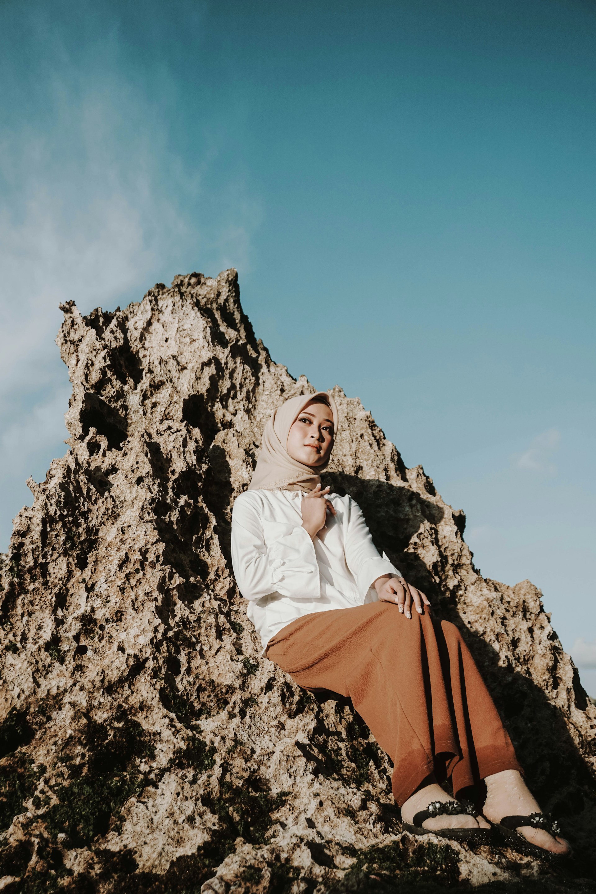 woman in white hijab and orange dress sitting on rock formation during daytime