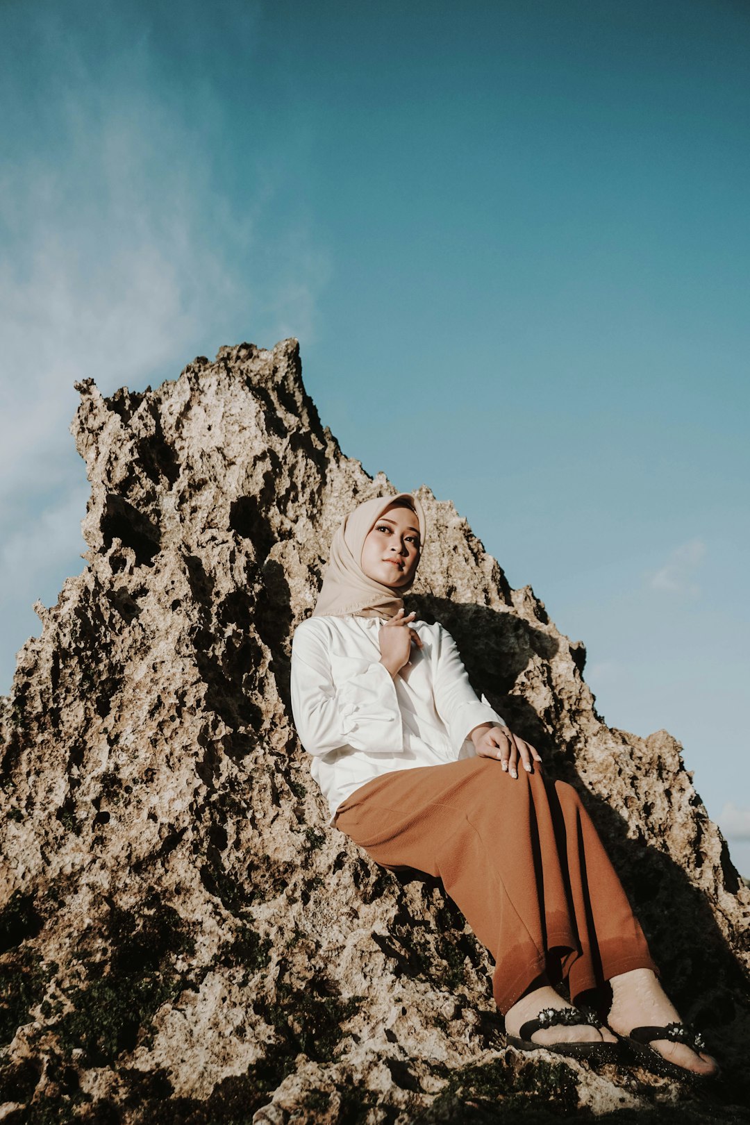 woman in white hijab and orange dress sitting on rock formation during daytime