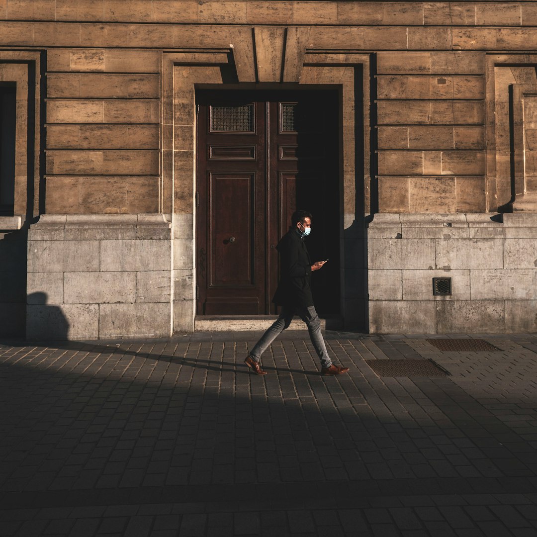 woman in black coat walking on sidewalk near brown wooden door