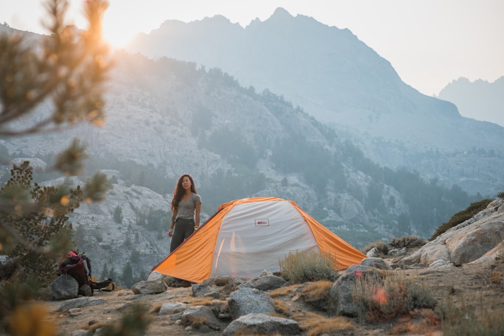 woman in gray jacket sitting on gray tent looking at mountains during daytime