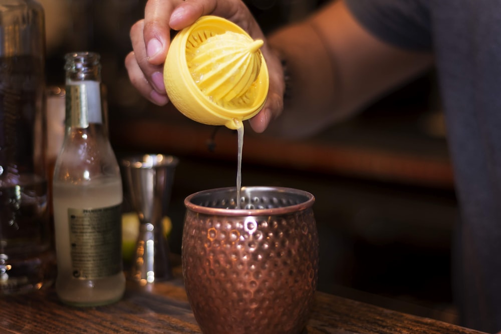 person pouring yellow lemon on clear drinking glass