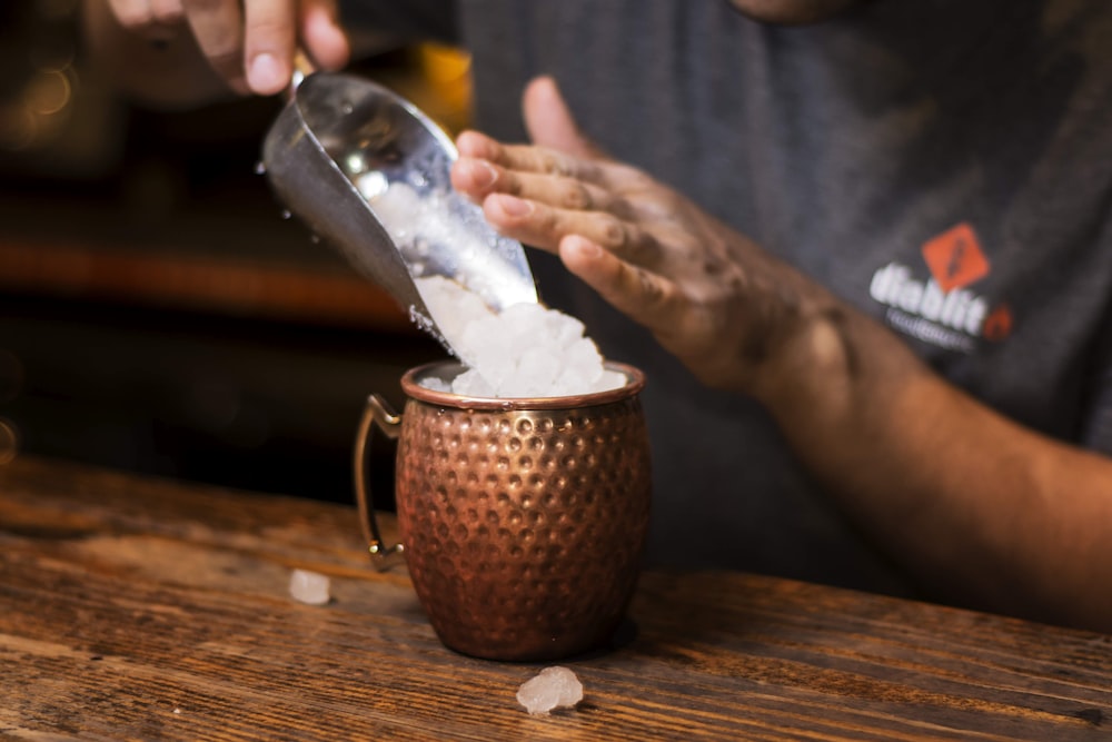 person pouring white powder on brown ceramic mug