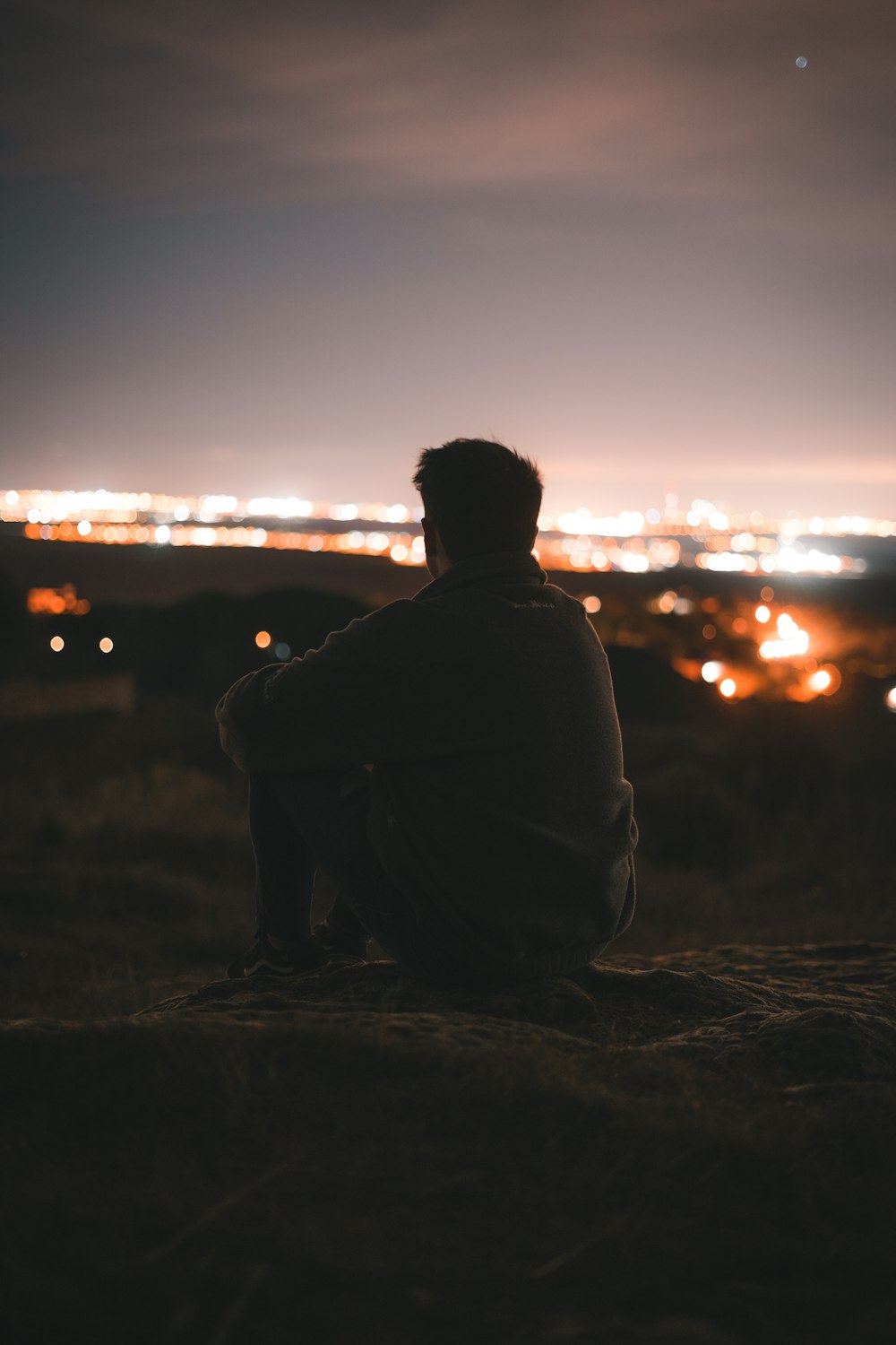 man in black jacket sitting on rock during sunset