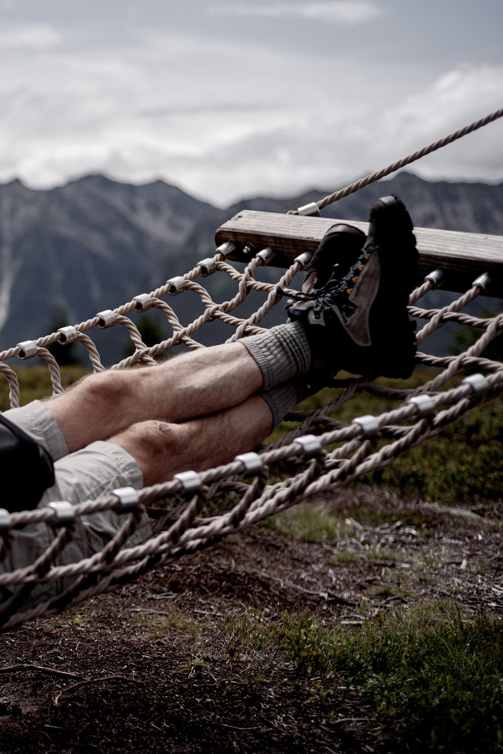 person in black and white sneakers lying on brown wooden swing during daytime