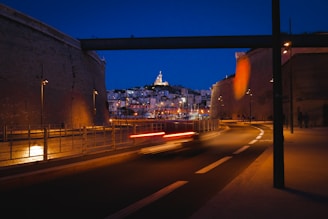 Nighttime cityscape viewed from a foggy hill road curve.
