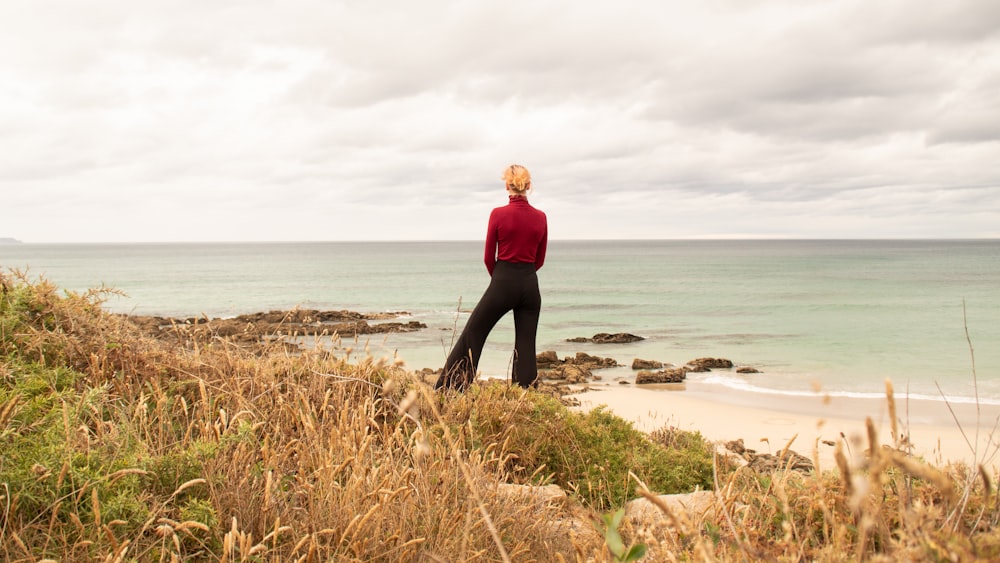 woman in red long sleeve shirt and black pants standing on brown sand near body of near near near near