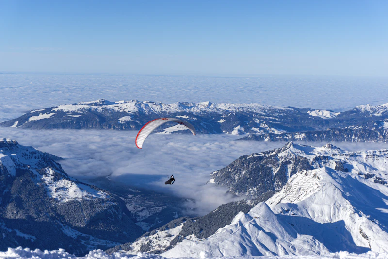 A paraglider soaring over the snow-covered Swiss Alps under a clear sky