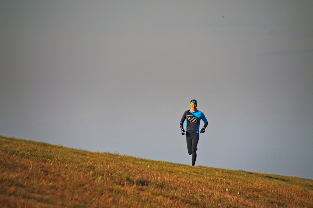man in blue jacket walking on brown grass field