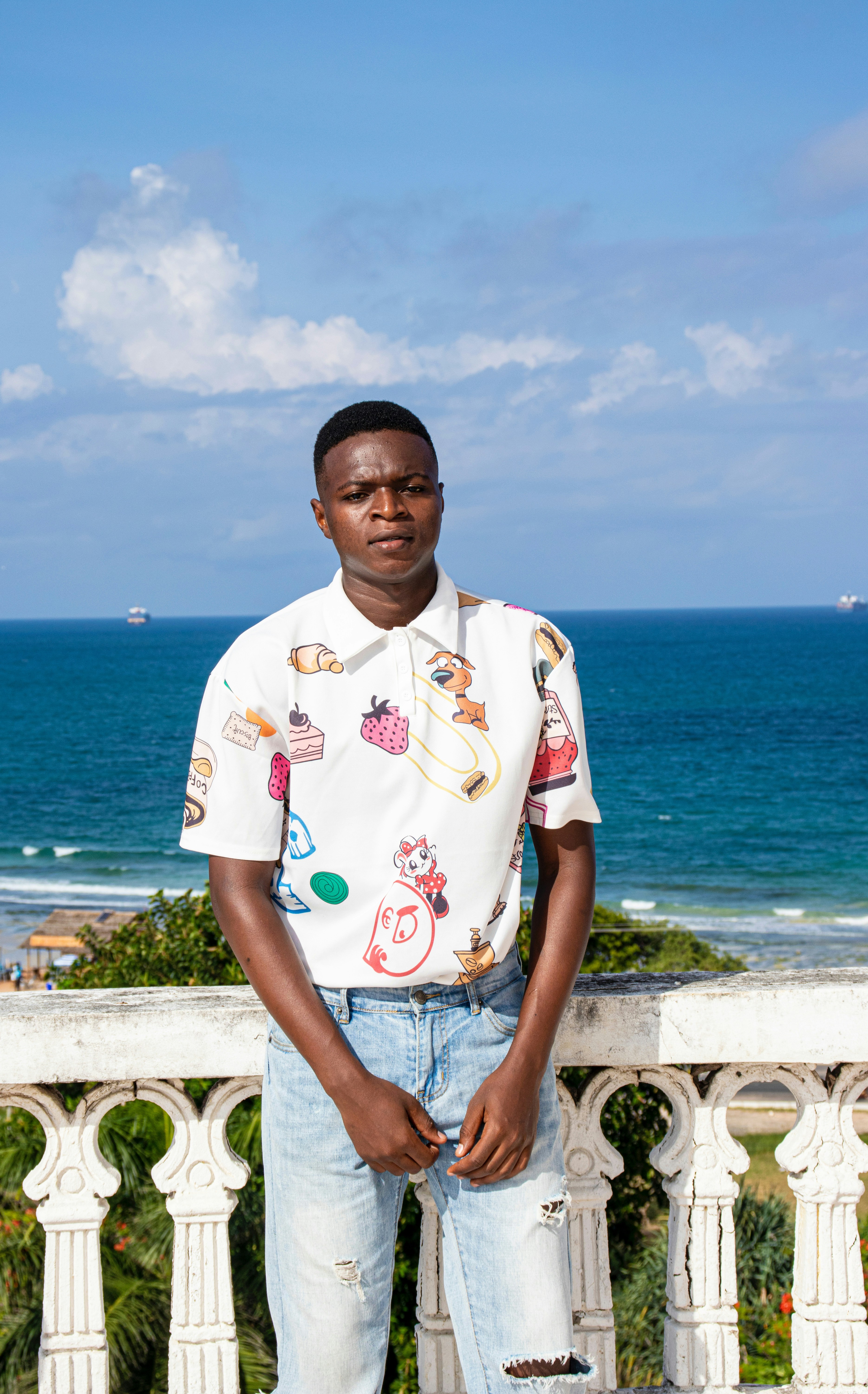 白と赤のポロシャツを着た男性が、水域近くの灰色のコンクリートフェンスの上に立っています