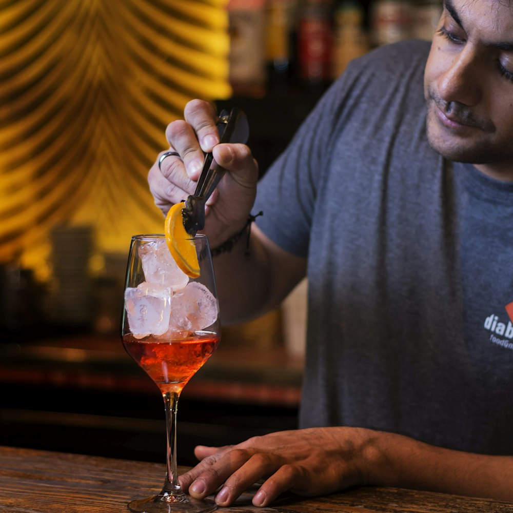 Hombre con camiseta gris de cuello redondo sosteniendo una copa de vino transparente