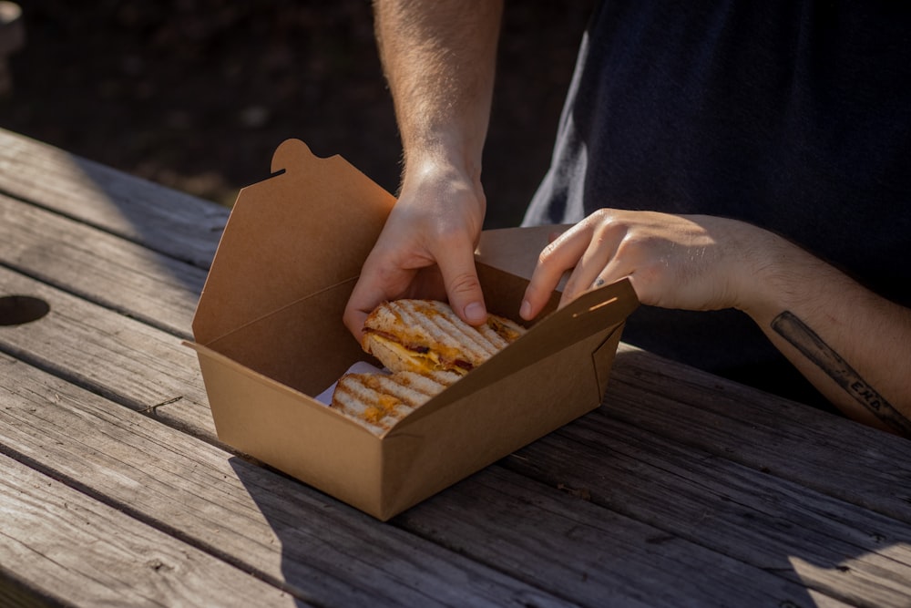 person holding brown box with brown and white food