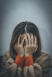 woman in brown sweater covering her face with her hand