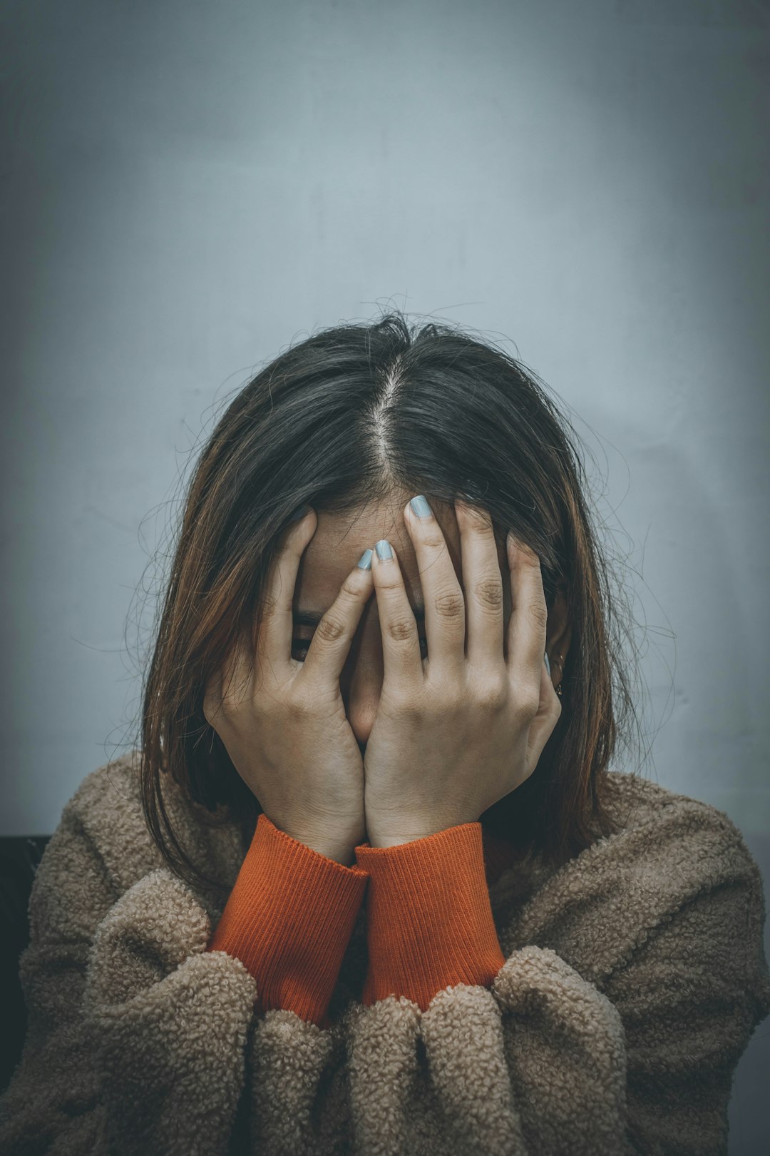 woman feeling angry in brown sweater covering her face with her hand