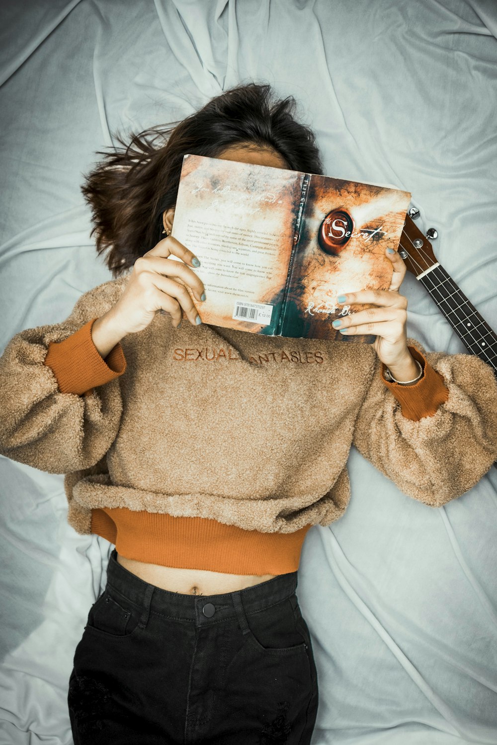 Frau in braunem Pullover und blauer Jeans spielt braune akustische Gitarre