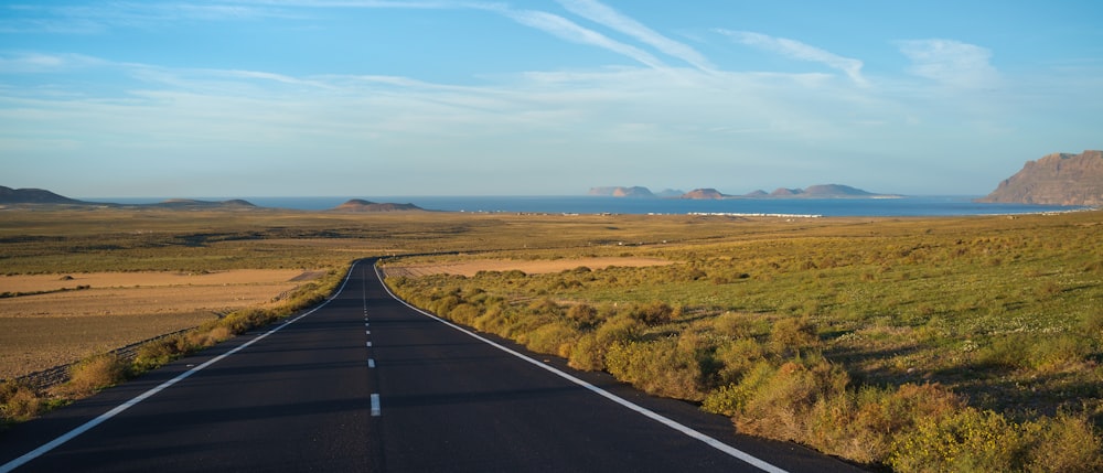 black asphalt road between green grass field under blue sky during daytime