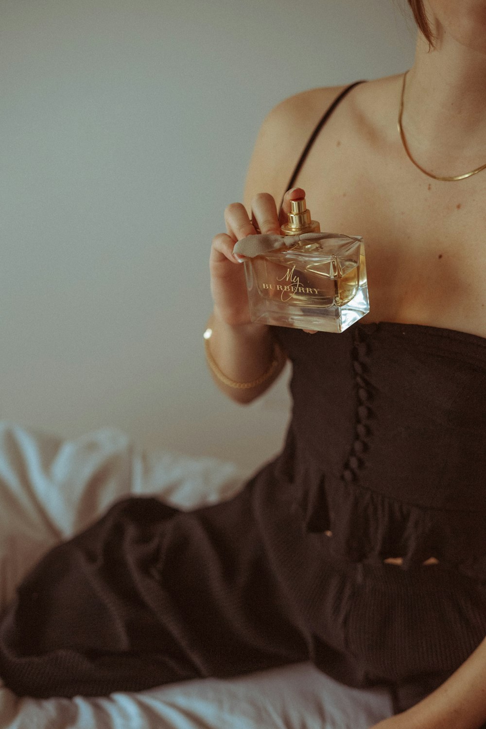 woman in black dress holding clear glass perfume bottle