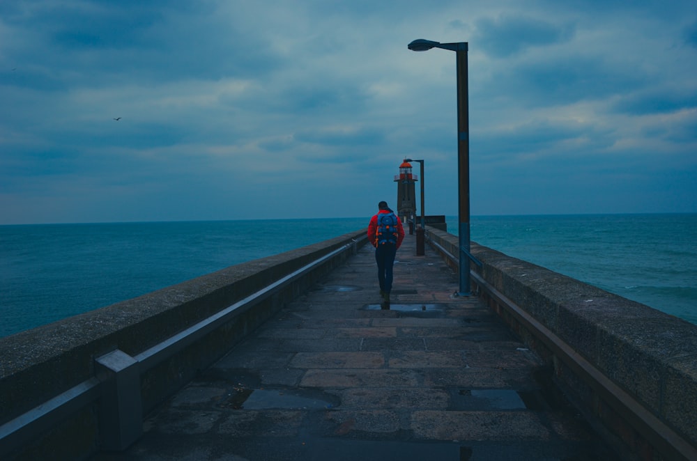 woman in red jacket and black pants walking on wooden dock during daytime