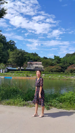 A smiling woman outdoors, taking a deep breath surrounded by green trees.