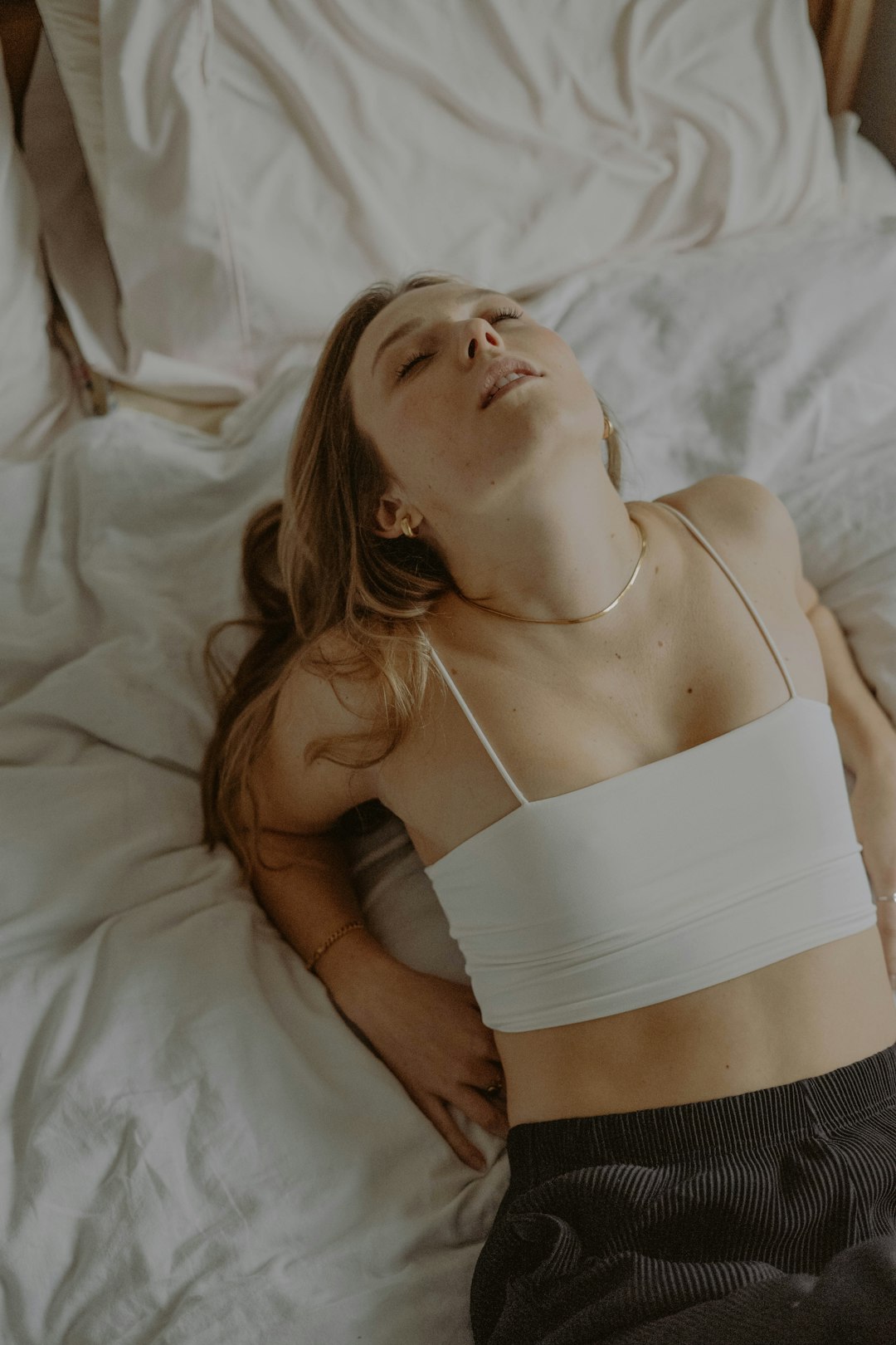 woman in white spaghetti strap top lying on bed