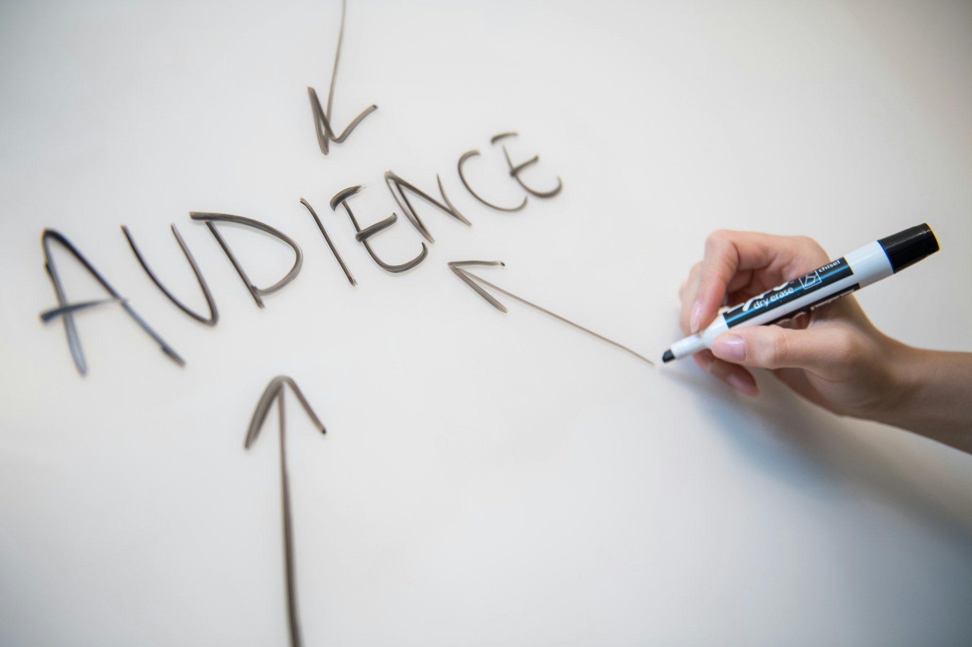 Woman's hand writing the word "audience" on a whiteboard, with arrows. 