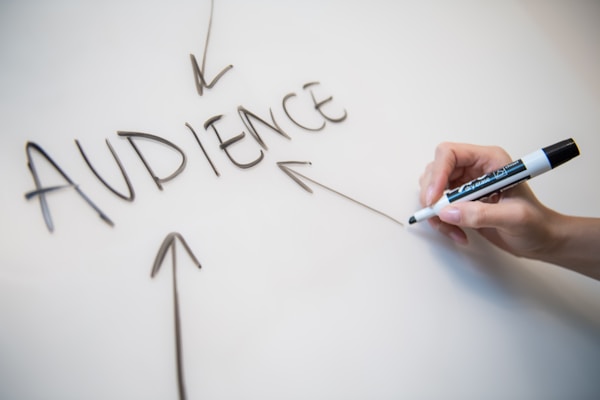 Woman's hand writing the word "audience" on a whiteboard, with arrows. by Melanie Deziel