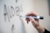 A hand is holding a black dry erase marker and writing the word 'AUDIENCE' on a whiteboard.