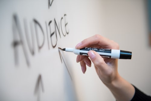 La palabra "Audiencia" escrita en una pizarra blanca y flechas apuntando hacia ella para representar audiencias atractivas en TikTok.