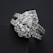 A close-up view of an elegant diamond ring featuring a large, pear-shaped central diamond surrounded by a halo of smaller round diamonds. The ring band is also adorned with diamonds, enhancing its luxurious appearance. The dark background contrasts with the brilliance of the diamonds, highlighting their sparkle.