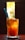 A tall glass filled with iced tea, garnished with orange slices, and accompanied by a blue straw and a spoon. The drink is backlit by bright sunlight, highlighting its amber color. The background is blurred, creating a focus on the refreshing beverage.
