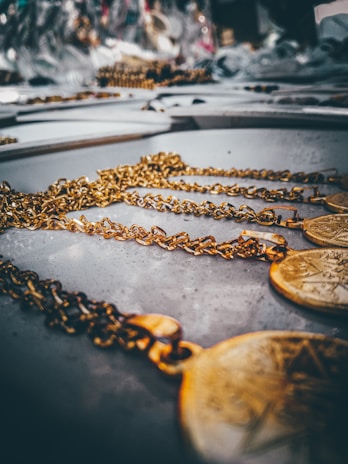 Golden chains with circular pendants are laid out on a flat surface, creating a sense of luxury and elegance. The focus is on the intricate details of the chains in the foreground, while the background softly blurs out.