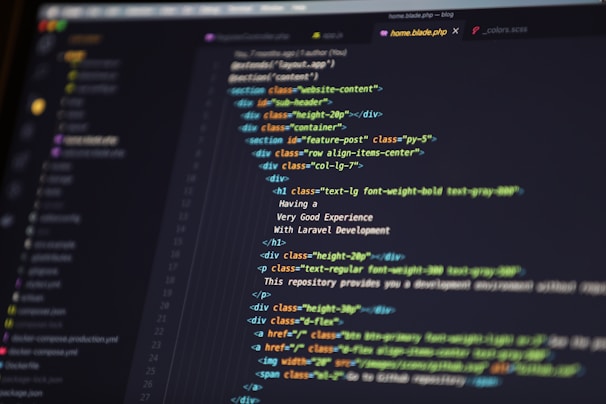 A close-up of a computer screen displaying HTML code in a text editor. The code includes elements such as sections, headers, and paragraphs, with various class attributes for styling. The interface shows file tabs at the top, suggesting it's part of a larger project.