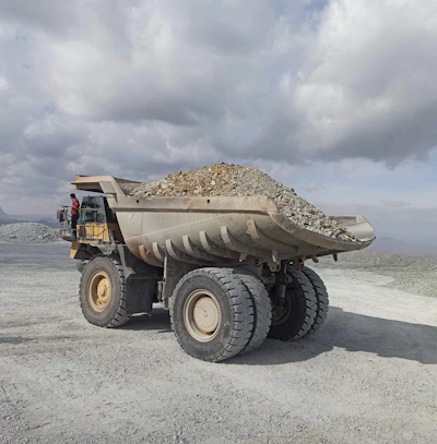 A JK Gravel dump truck unloading fresh pea gravel at a customer's driveway surrounded by lush greenery.