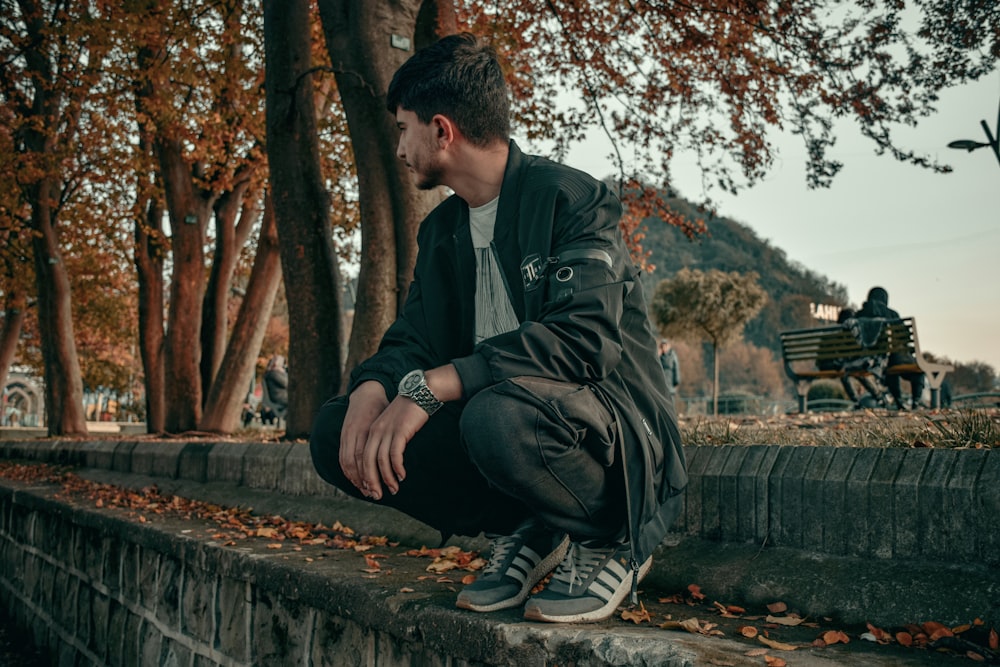 man in black jacket sitting on concrete bench during daytime