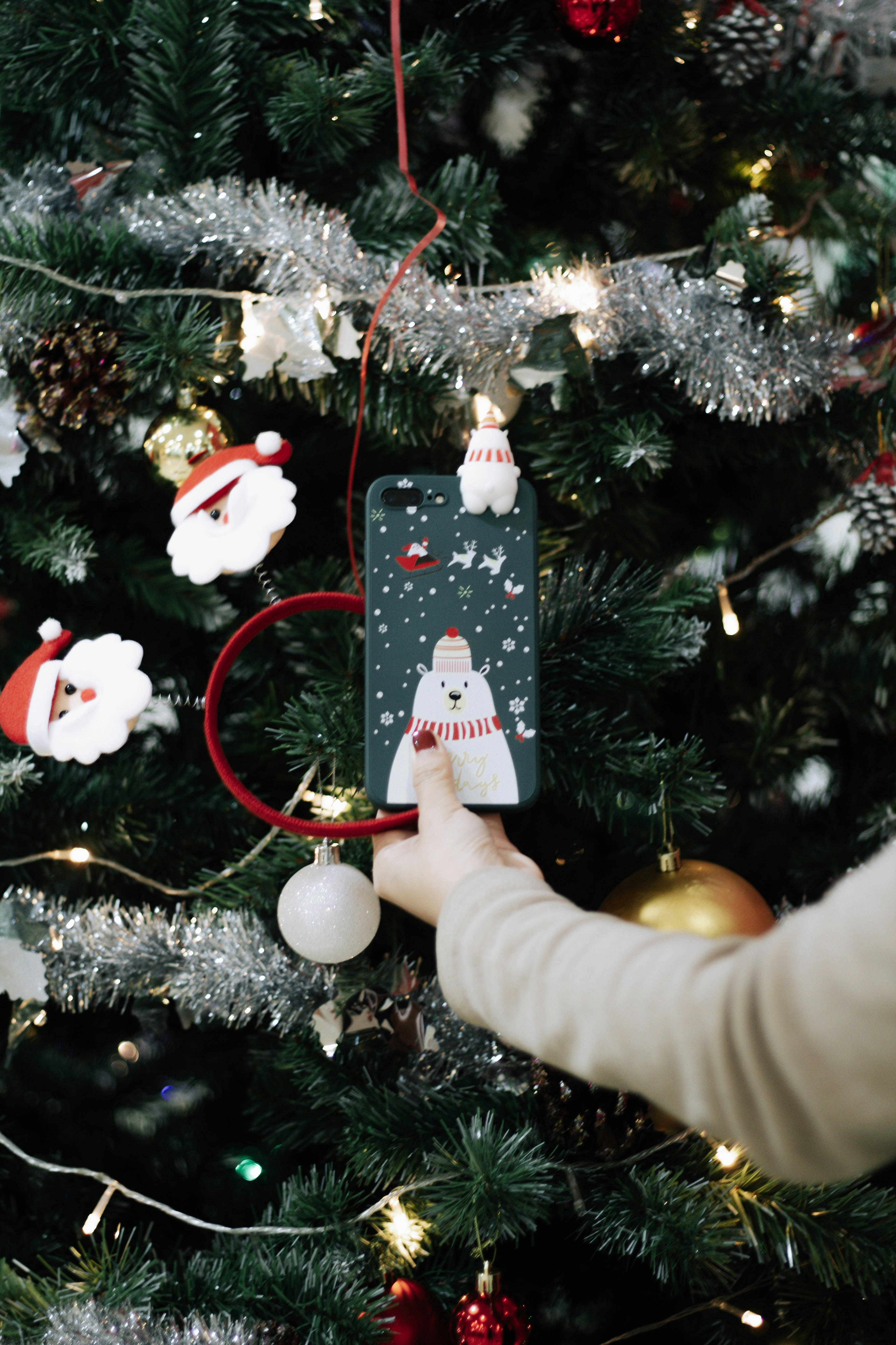 A CASELAB Christmas phone case hung on a decorated tree beside a gold ornament
