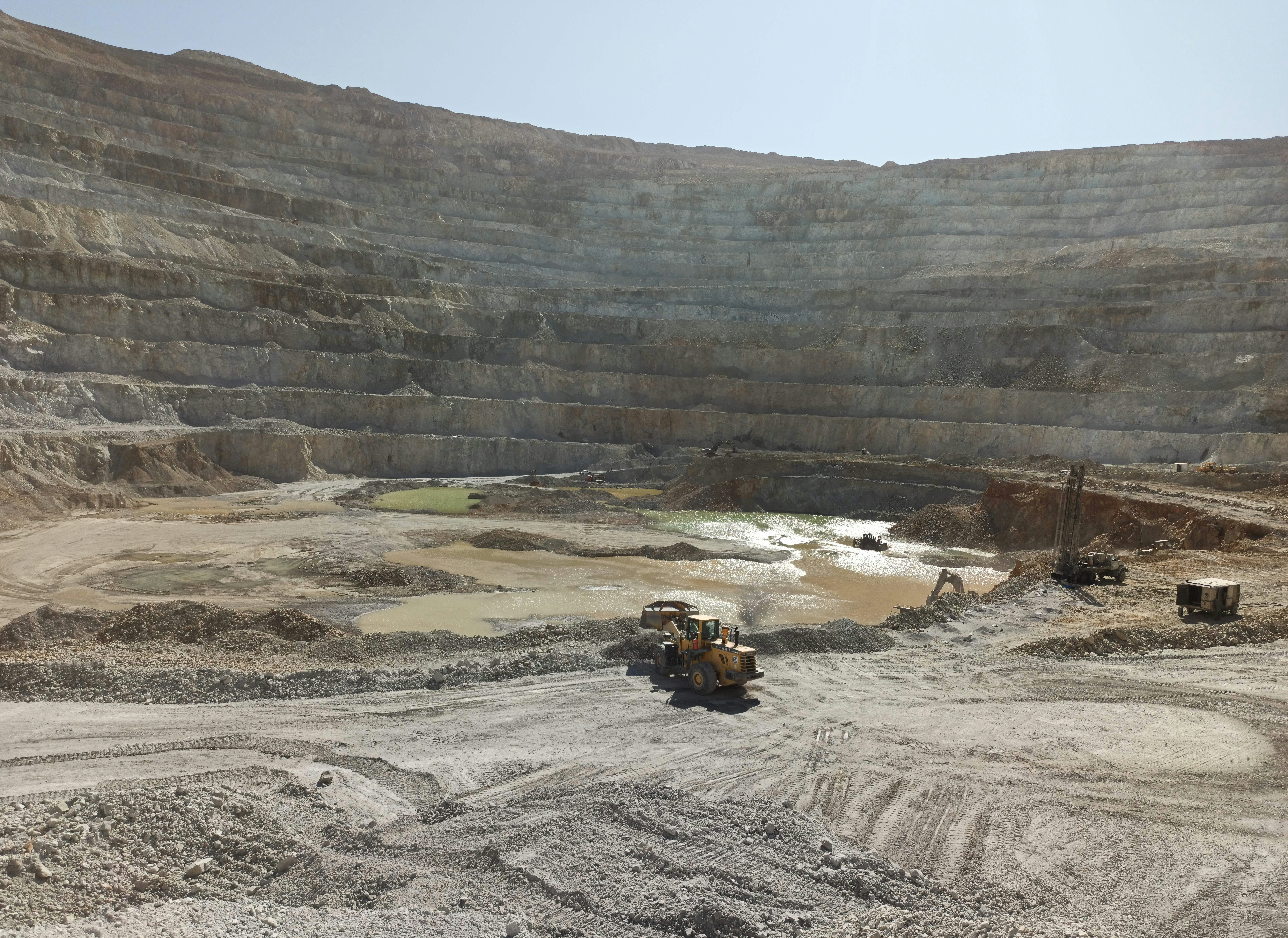 Large yellow excavator operating in an open-pit mine in East Africa with terraced walls and dust clouds