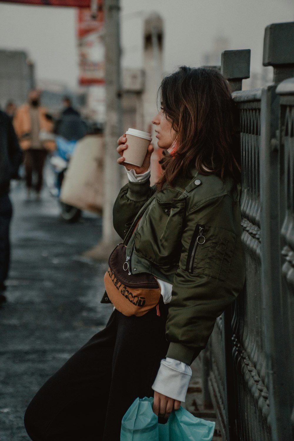 woman in green jacket holding white ceramic mug