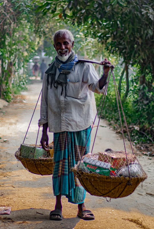 man in gray dress shirt and red and black plaid pants holding brown woven basket in Dhaka Bangladesh