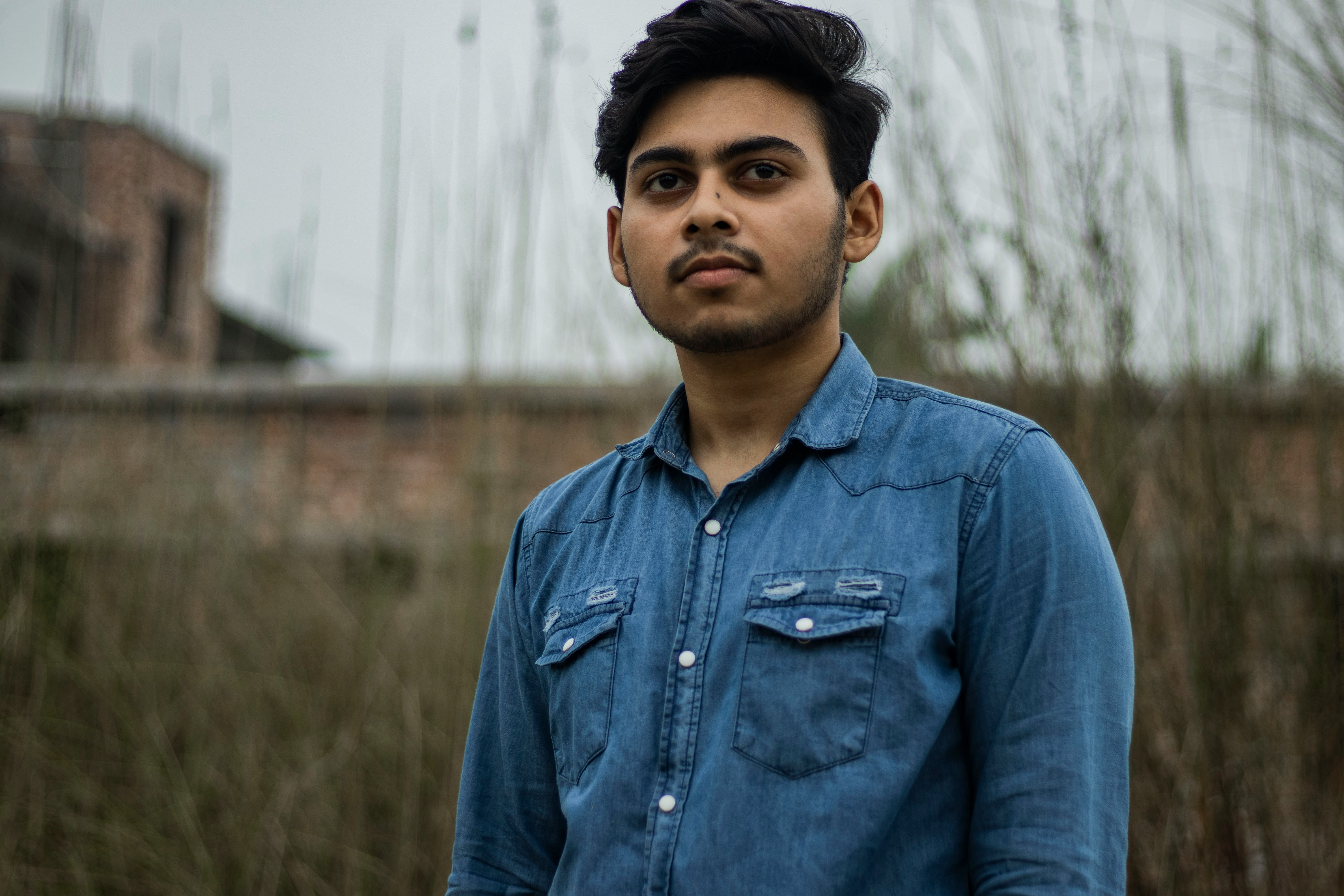 man in blue denim button up jacket standing near green grass during daytime