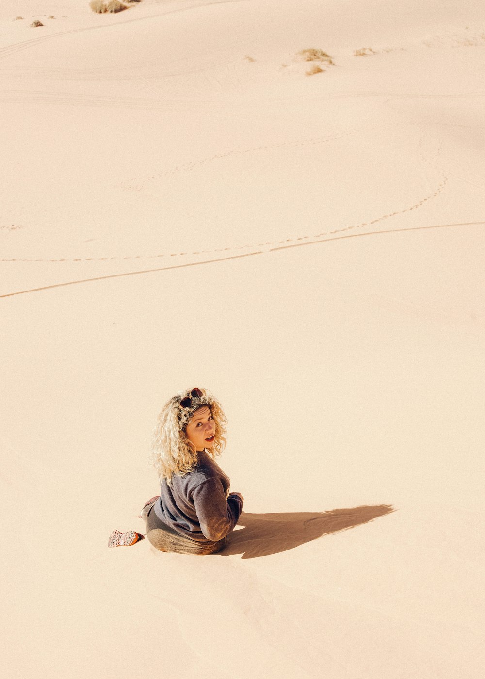 woman in blue long sleeve shirt sitting on white sand during daytime